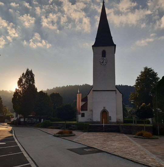 Eine weiße Kirche mit einem hohen Glockenturm und einem dunklen Kirchturm steht an einer Straße.